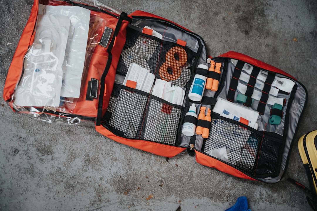 An open red medical bag filled with various supplies on a grey surface