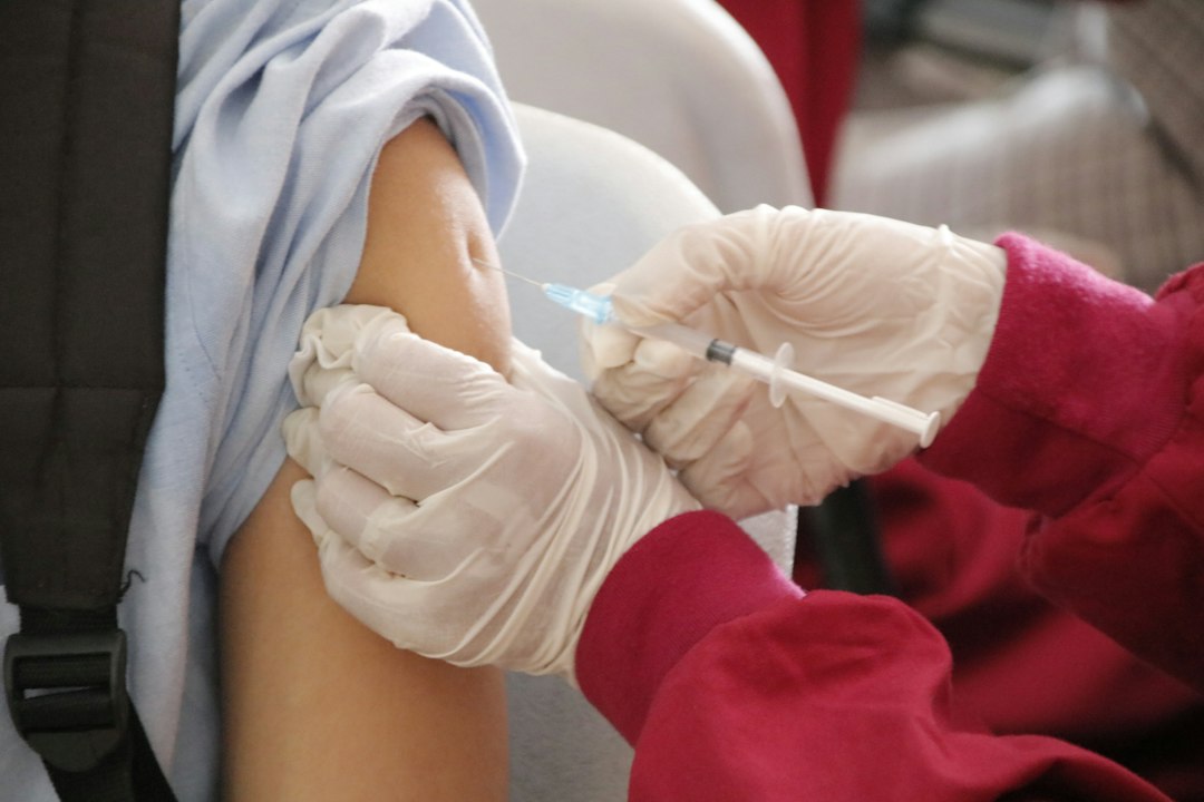 a person in a red shirt and white gloves receiving a vaccine