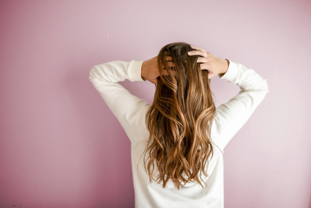 woman examining her hair in front of a pink wall